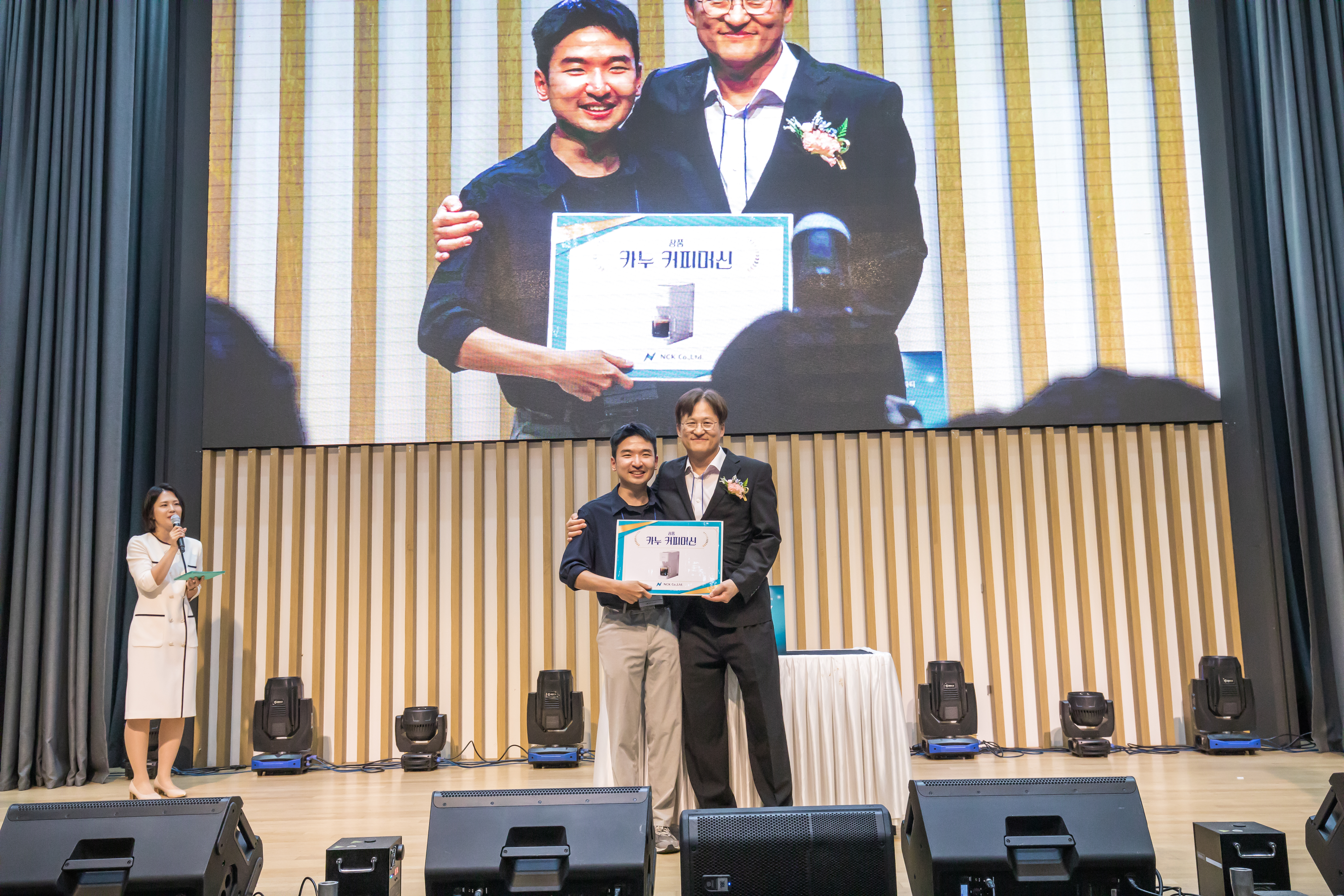 창립기념식 식순 중 시상 순서에서 무대 위 수상자와 대표가 함께 서고 화면에 장면이 중계되는 모습
